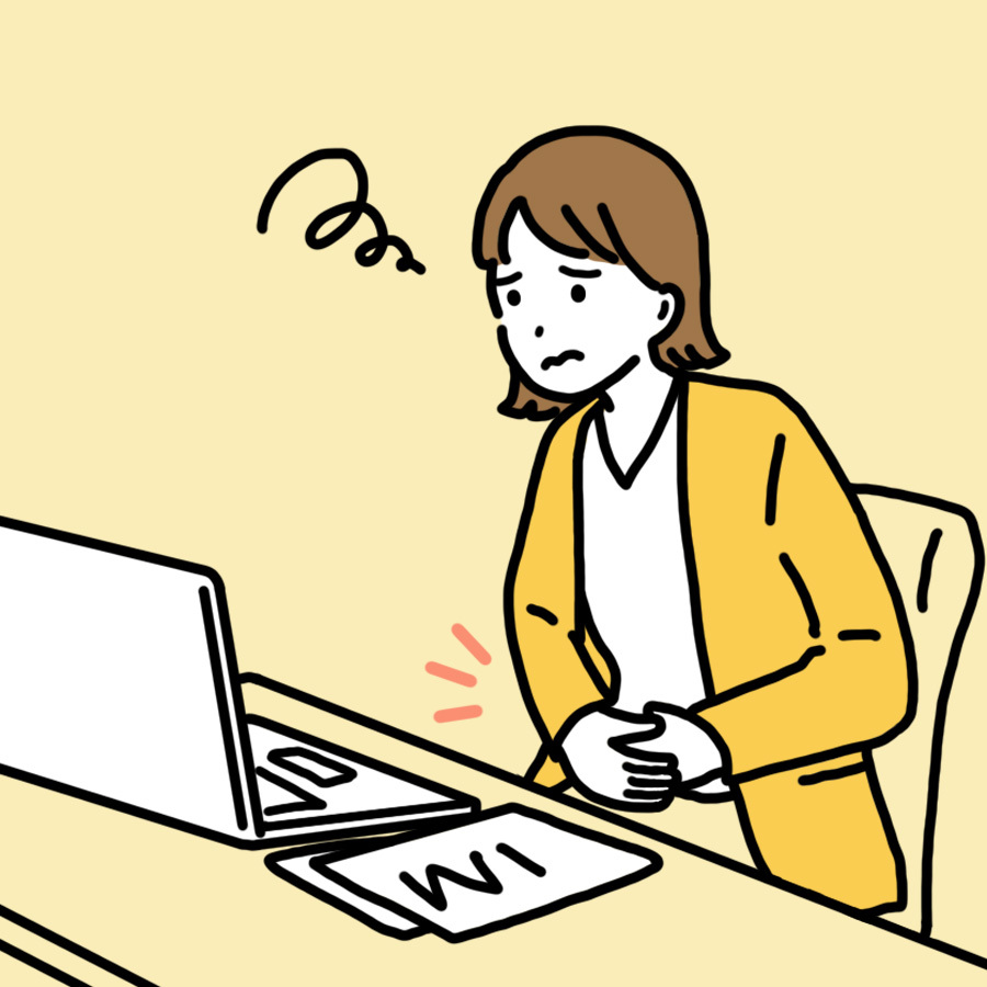 PCで仕事中にお腹の張りに悩む若い女性。