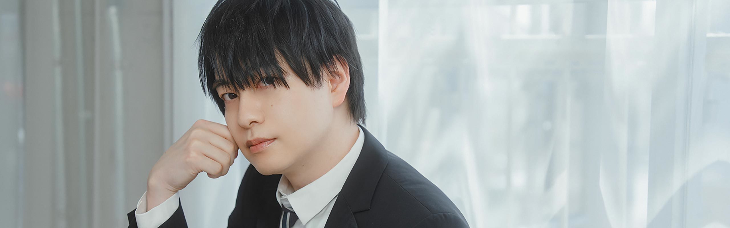 スーツ姿で、カメラ目線の声優の小林さん。