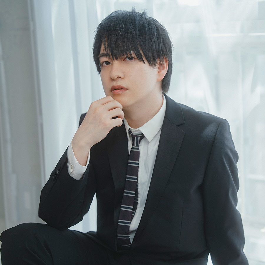 スーツ姿で、カメラ目線の声優の小林さん。