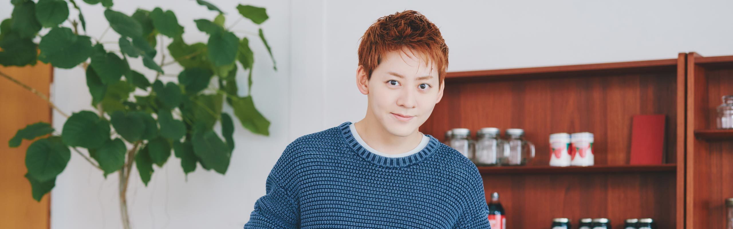 食器棚を背景にカメラを見つめる牧島さん。