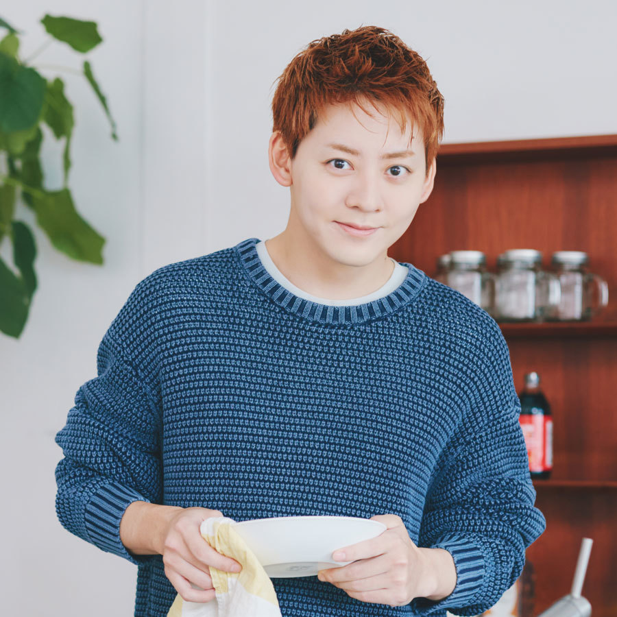 食器棚を背景にカメラを見つめる牧島さん。