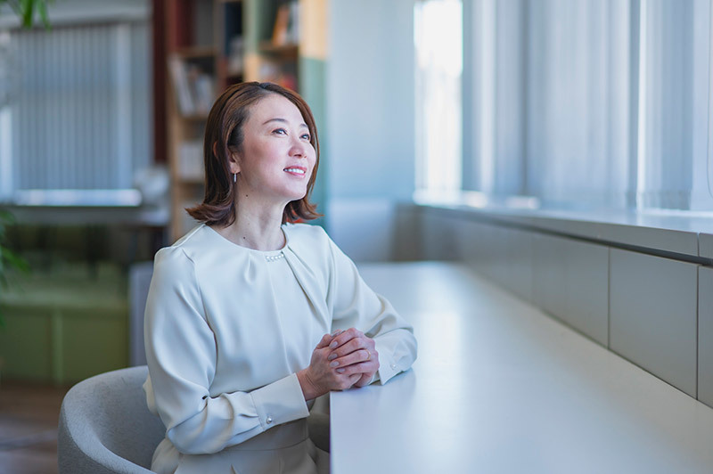 窓際の椅子に座り外を見つめる田中雅美さん。