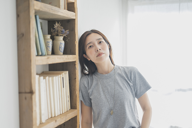 本棚の横でカメラに向かってポーズをとるharu.さん。
