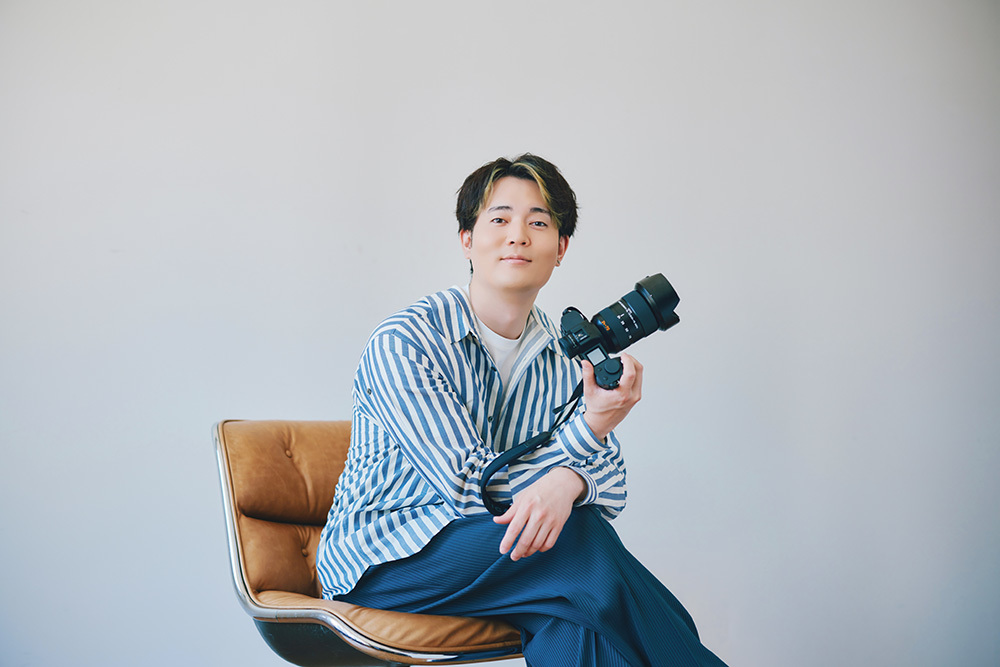 椅子に座りカメラを持つ駒田さん。