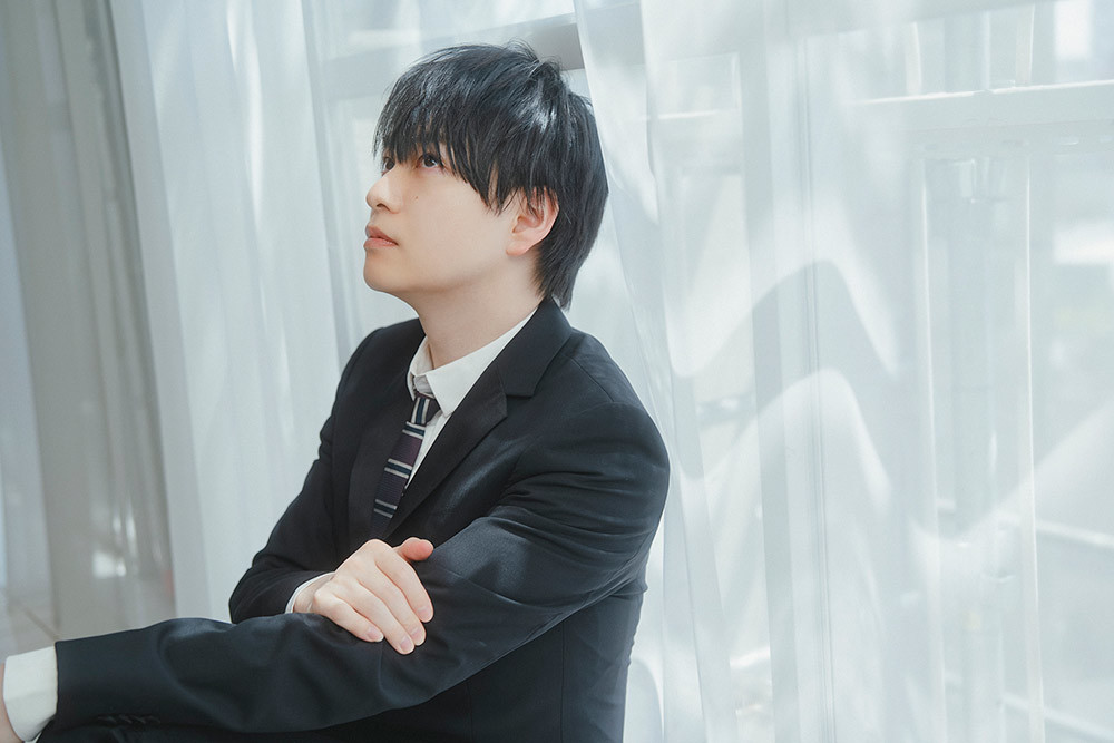 窓際にもたれる声優の小林さん。