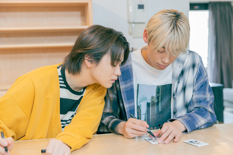 チェキにサインする髙松アロハさんをのぞき込む大倉空人さん。