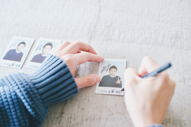チェキにサインをする牧島さんの手元。