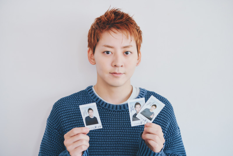 サイン入りチェキを手にカメラを見つめる牧島さん。