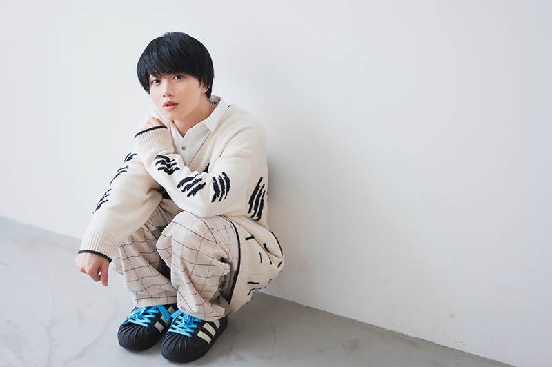 しゃがんで壁にもたれながらカメラ目線を向ける植田さん。